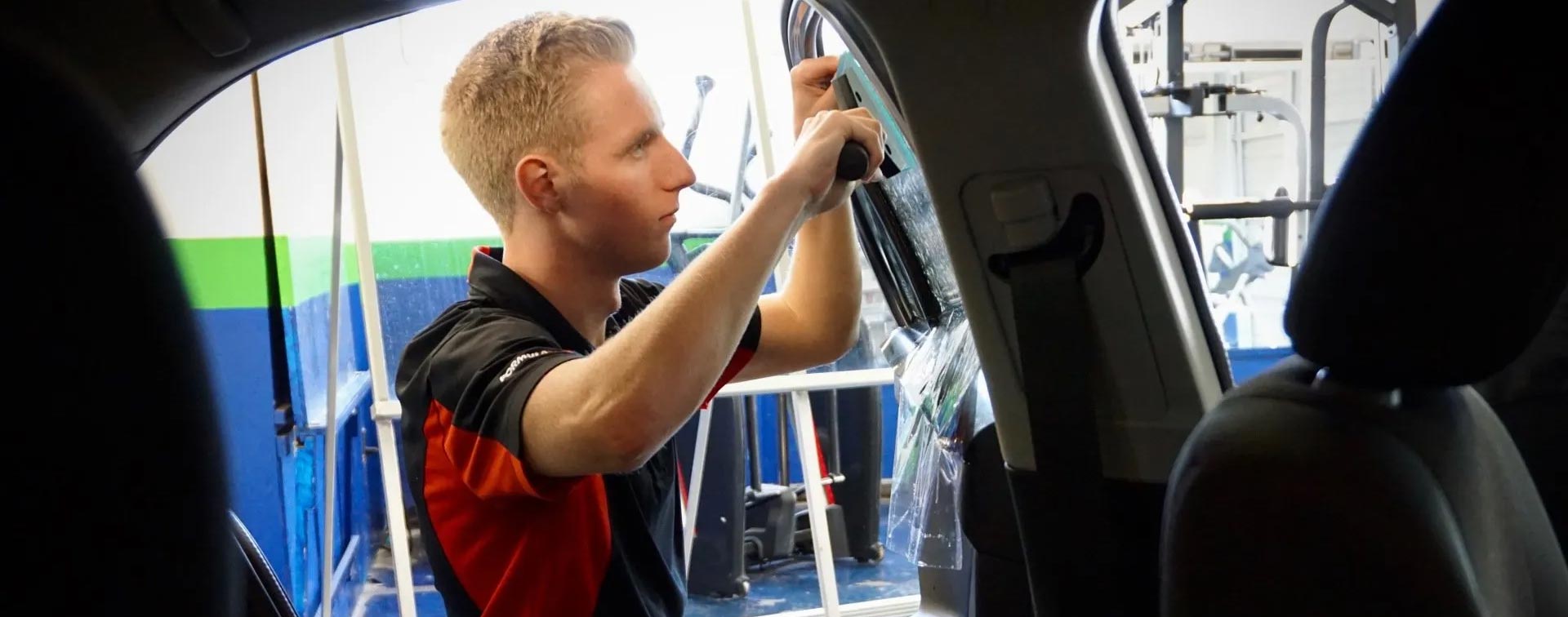 A man is working on a car window with a tool.