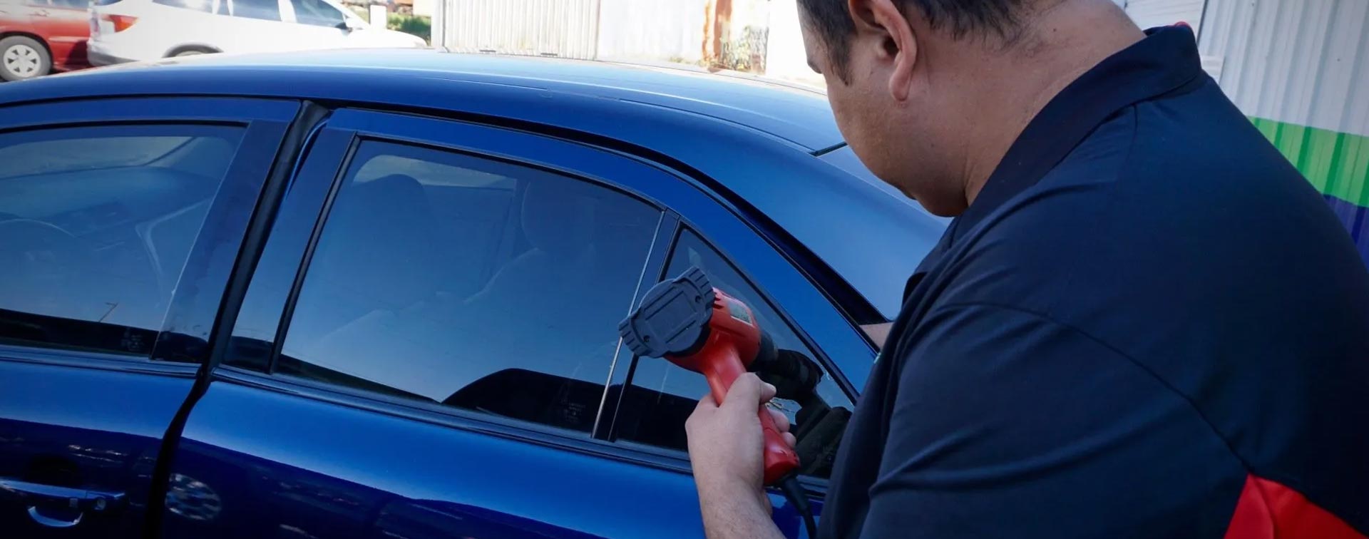 A man is applying window tinting to a blue car.