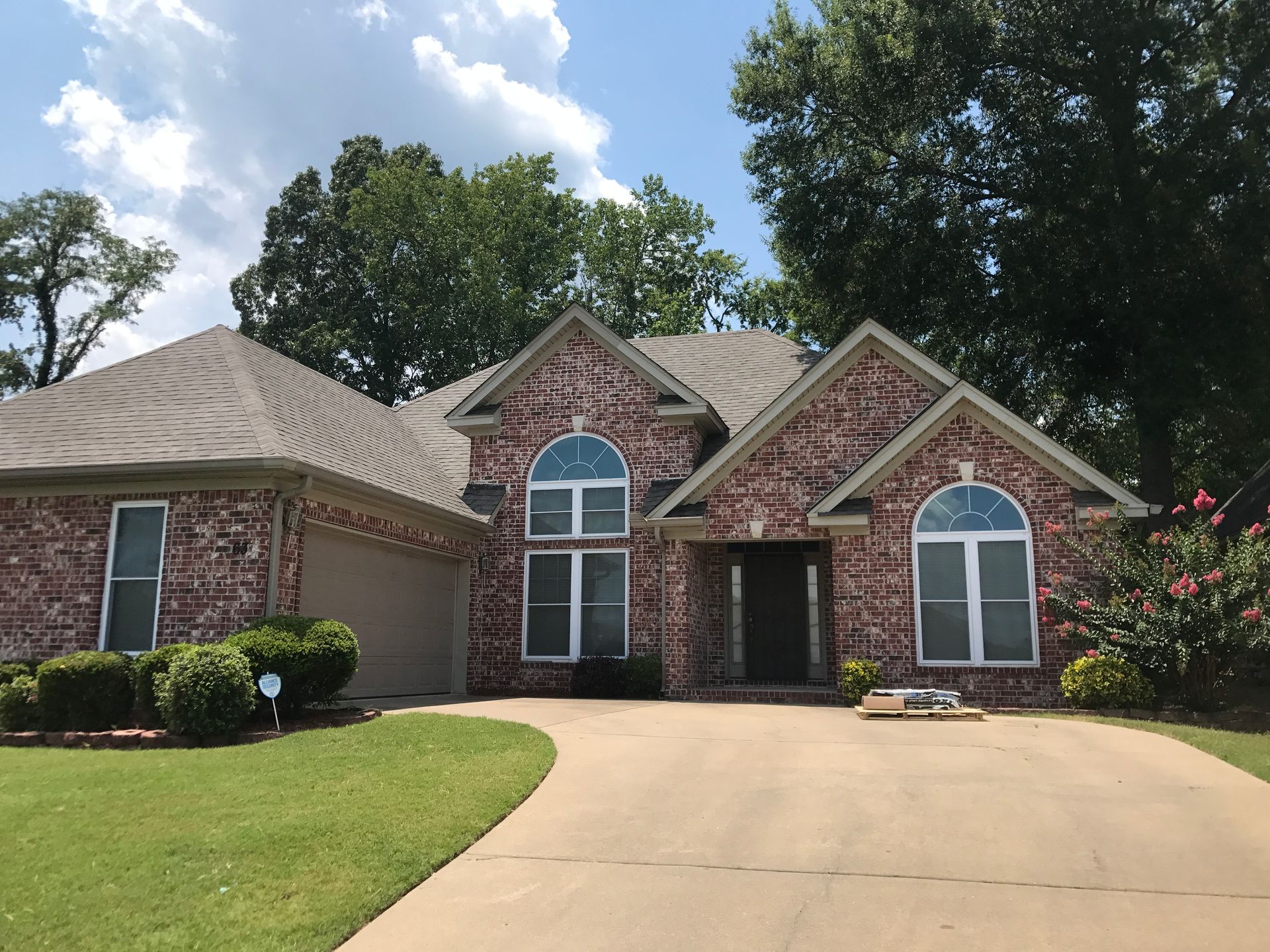 Brick house with arched windows, garage, and driveway under a blue sky.