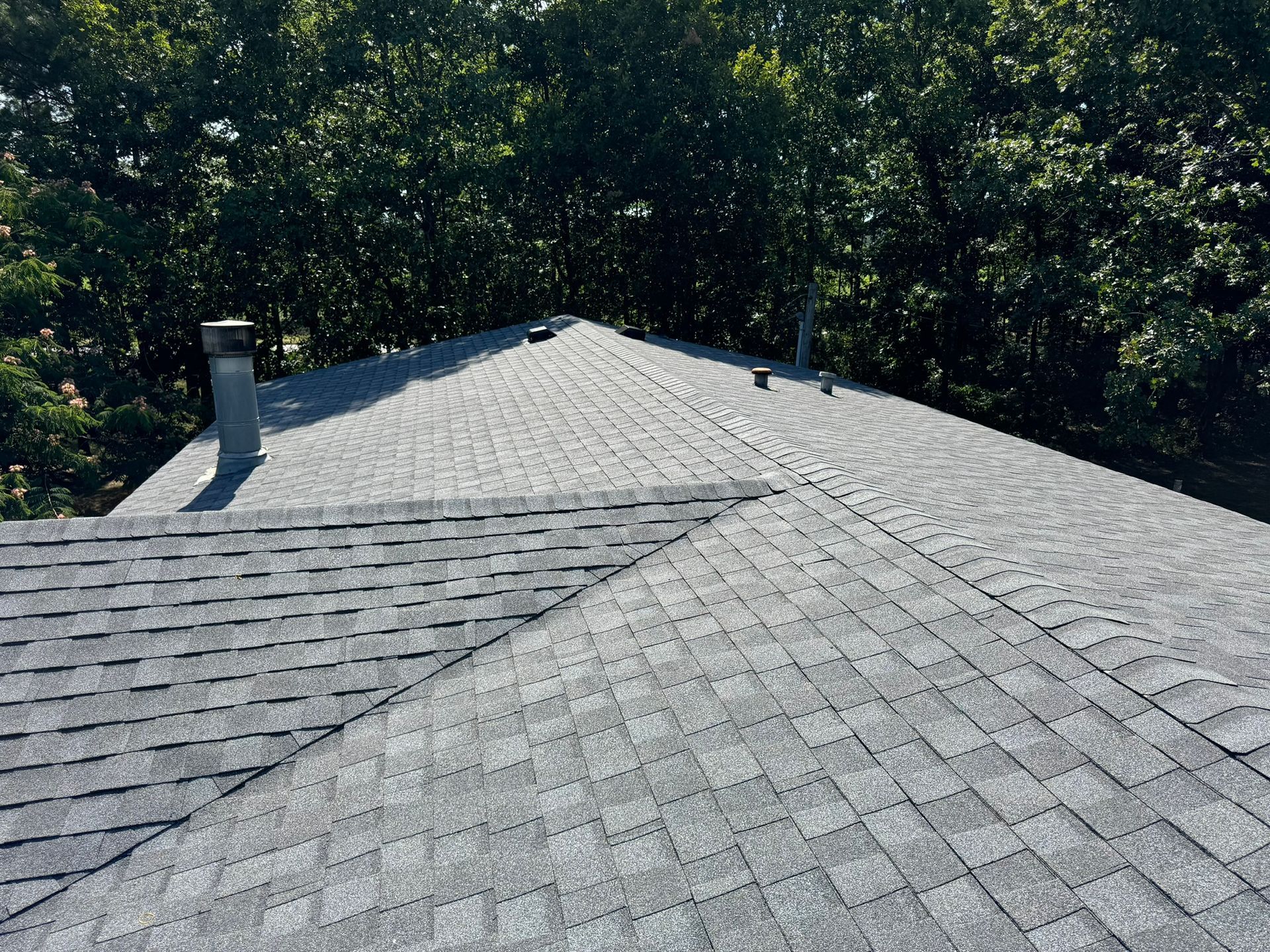 Gray asphalt shingle roof on a house with trees in the background.