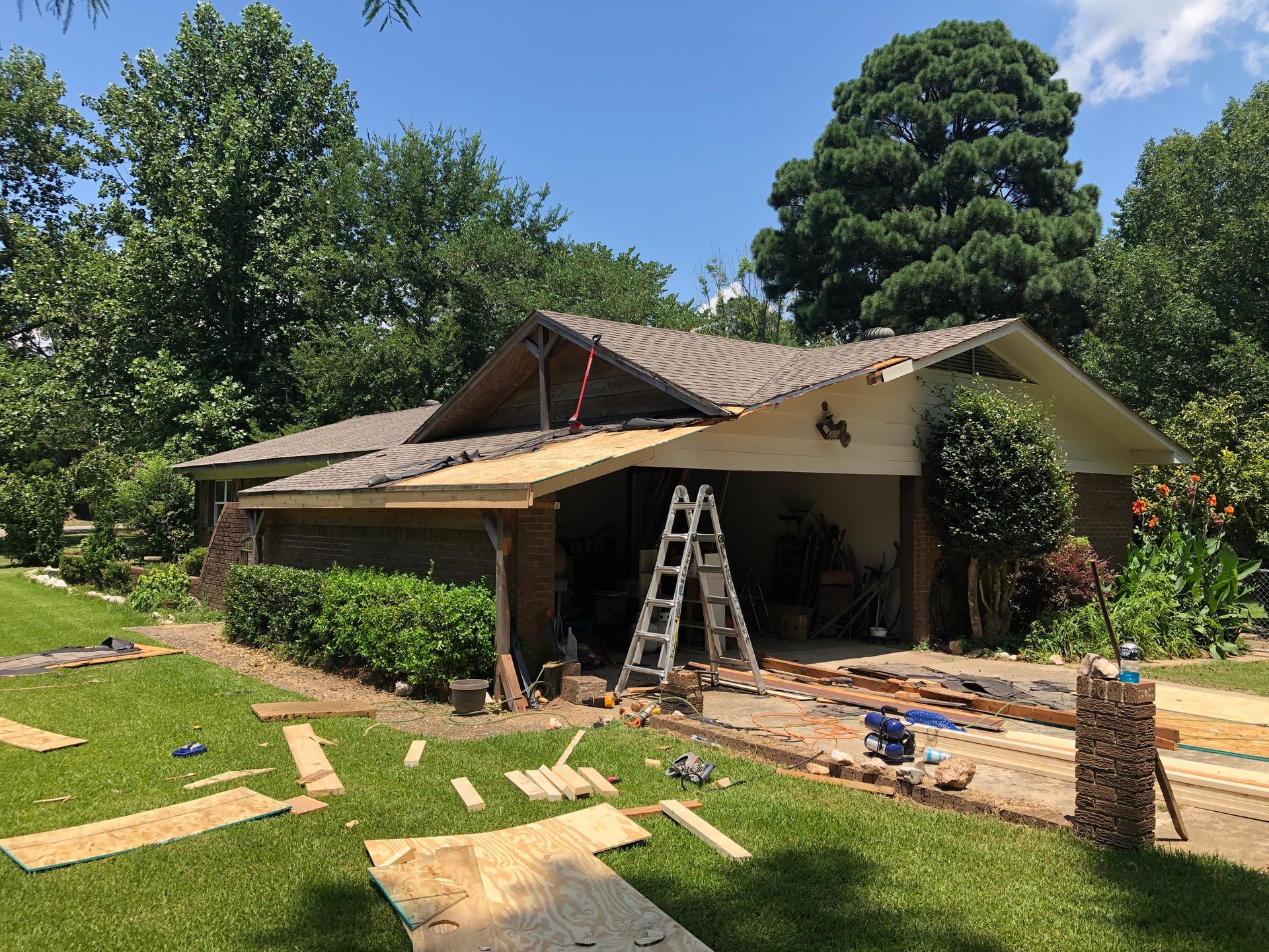 House with roof construction in progress, ladder, materials on the ground, sunny day.