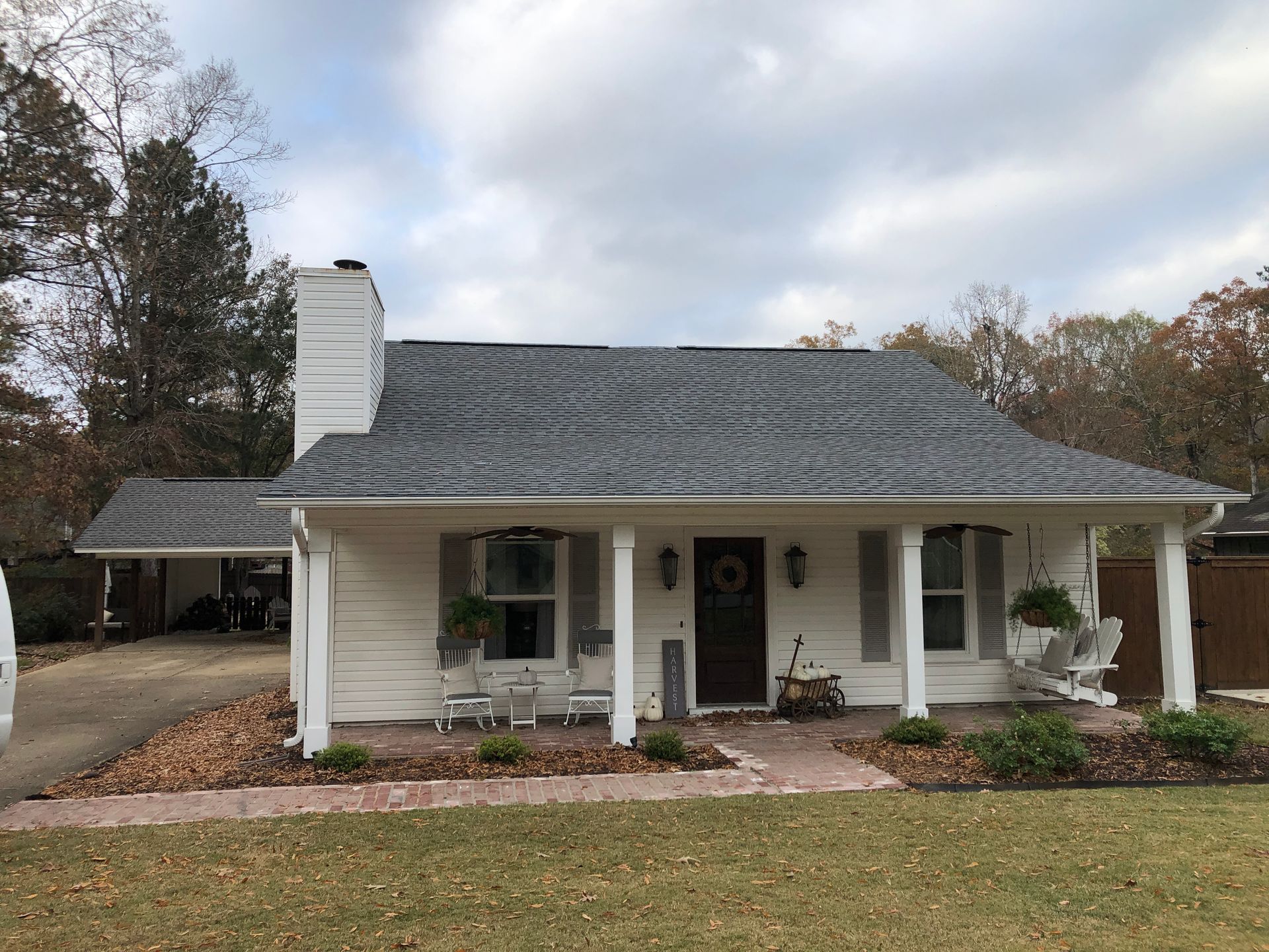 White house with gray roof, porch, and a carport. Brown door with a wreath.