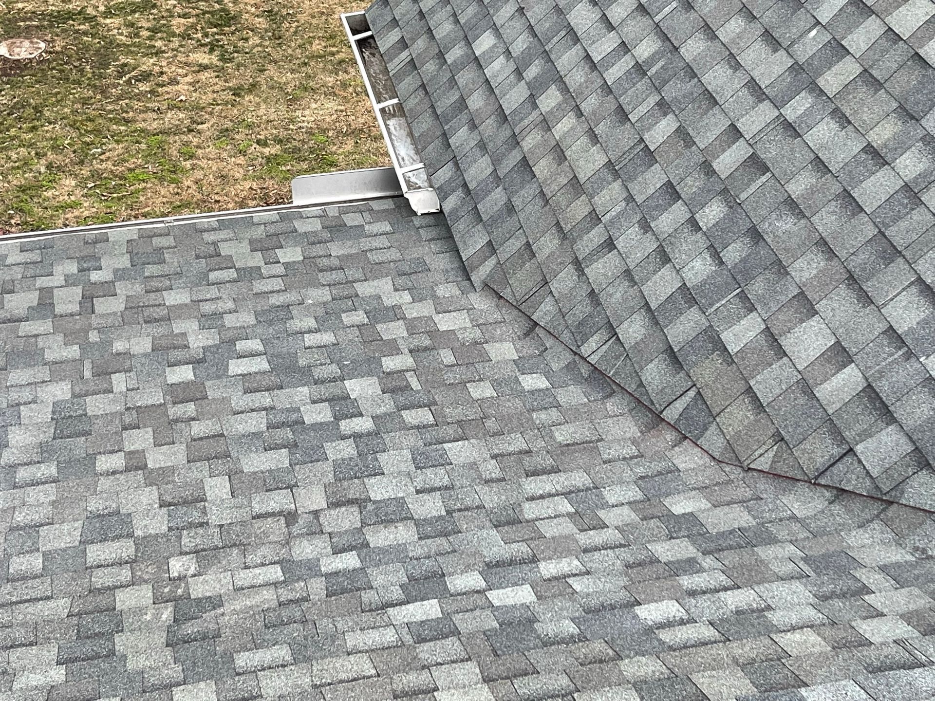 Overhead view of two gray asphalt shingle roof sections meeting, near a gutter.