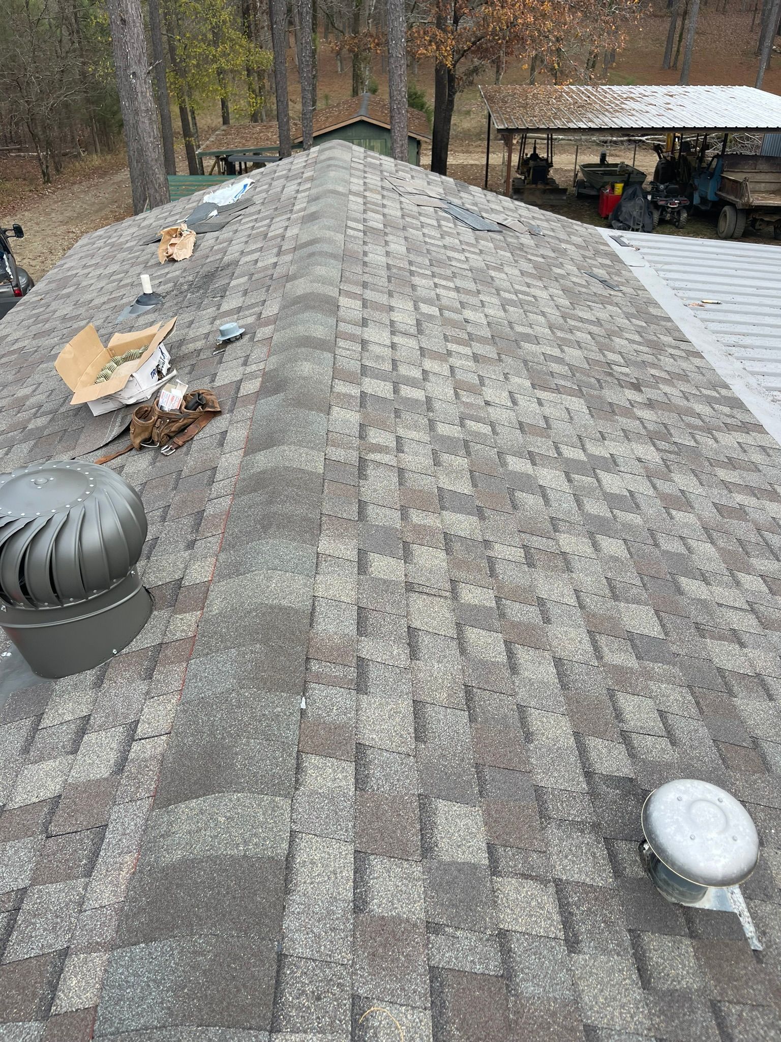 Close-up of a shingled roof with a vent and debris scattered on it. The roof is brown and gray.