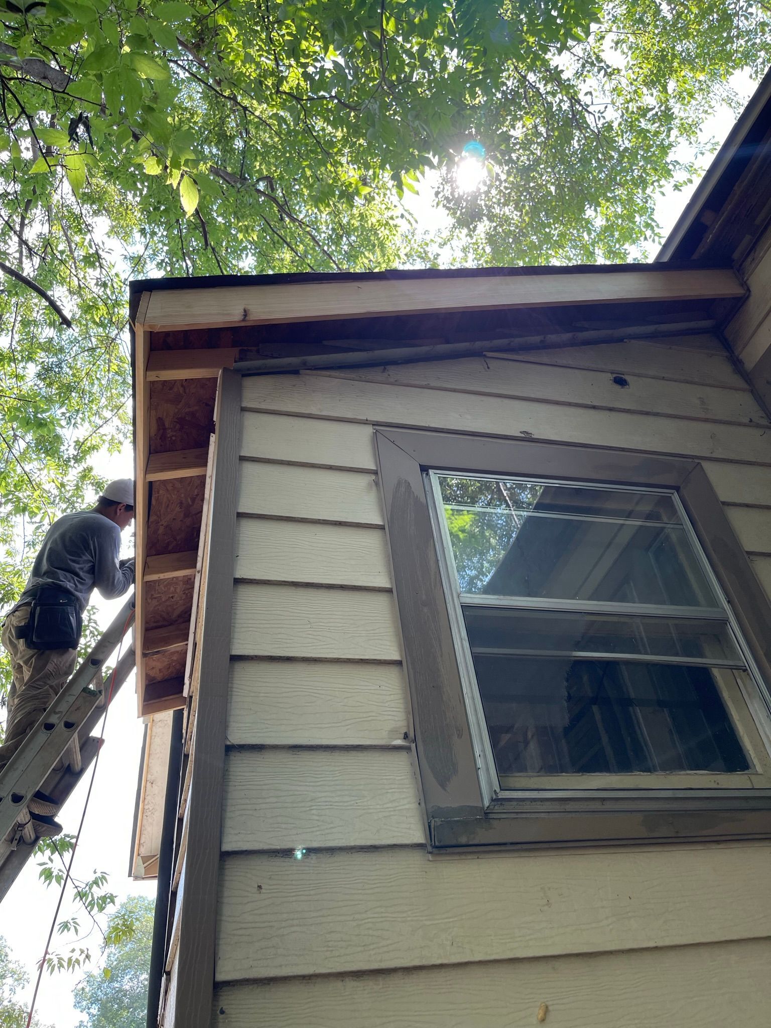 Person on ladder repairs house siding near a window.