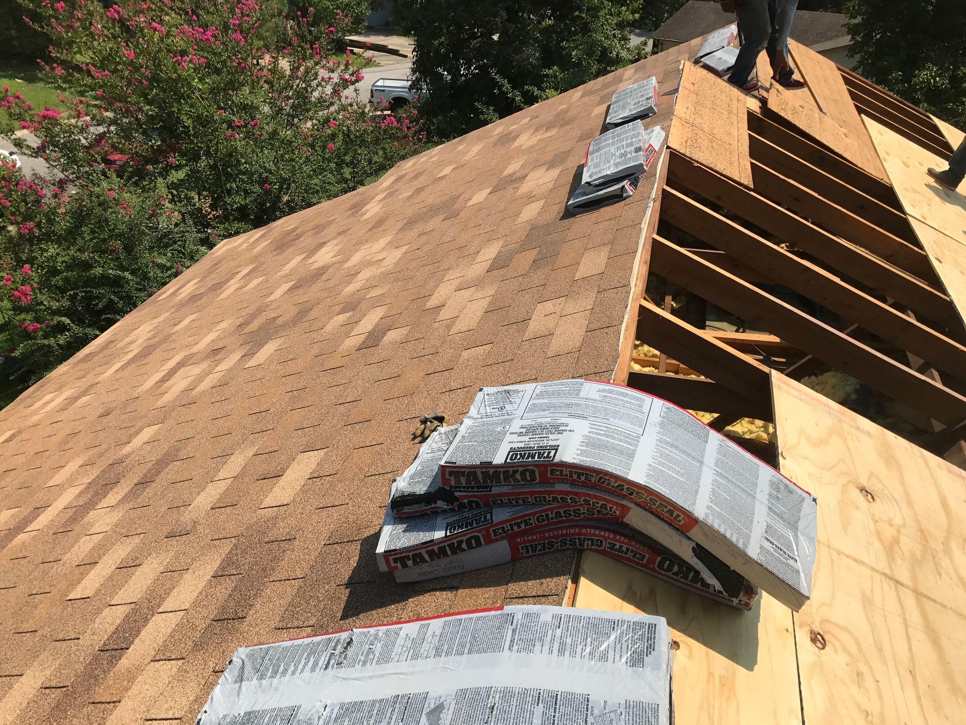 Roofers working on a partially shingled roof, with stacks of shingles and exposed wood.