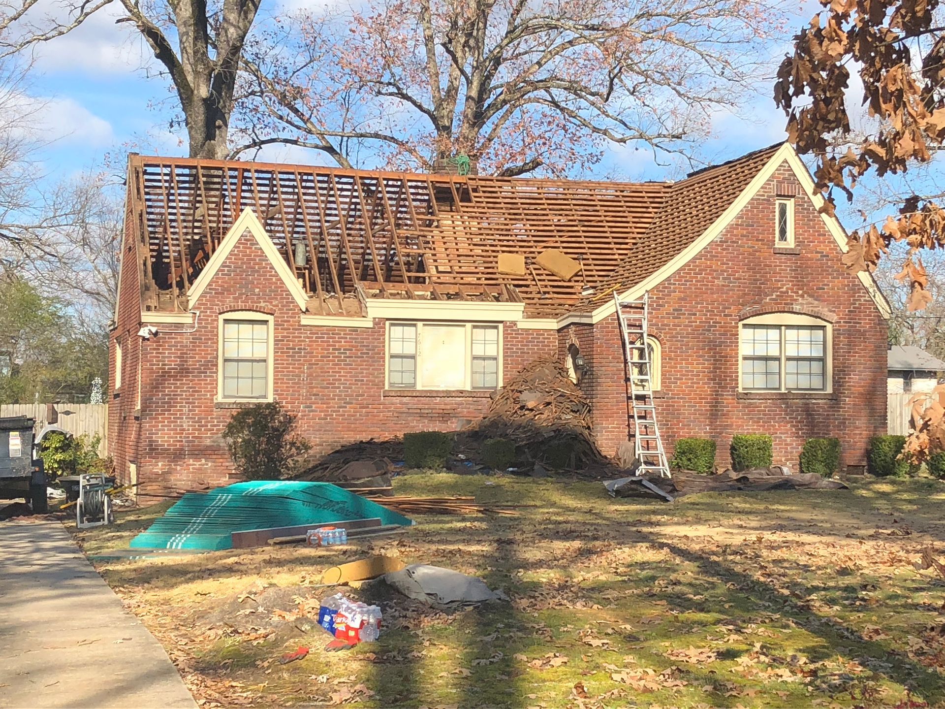 Brick house with roof partially removed during renovation; ladder leaning against it.