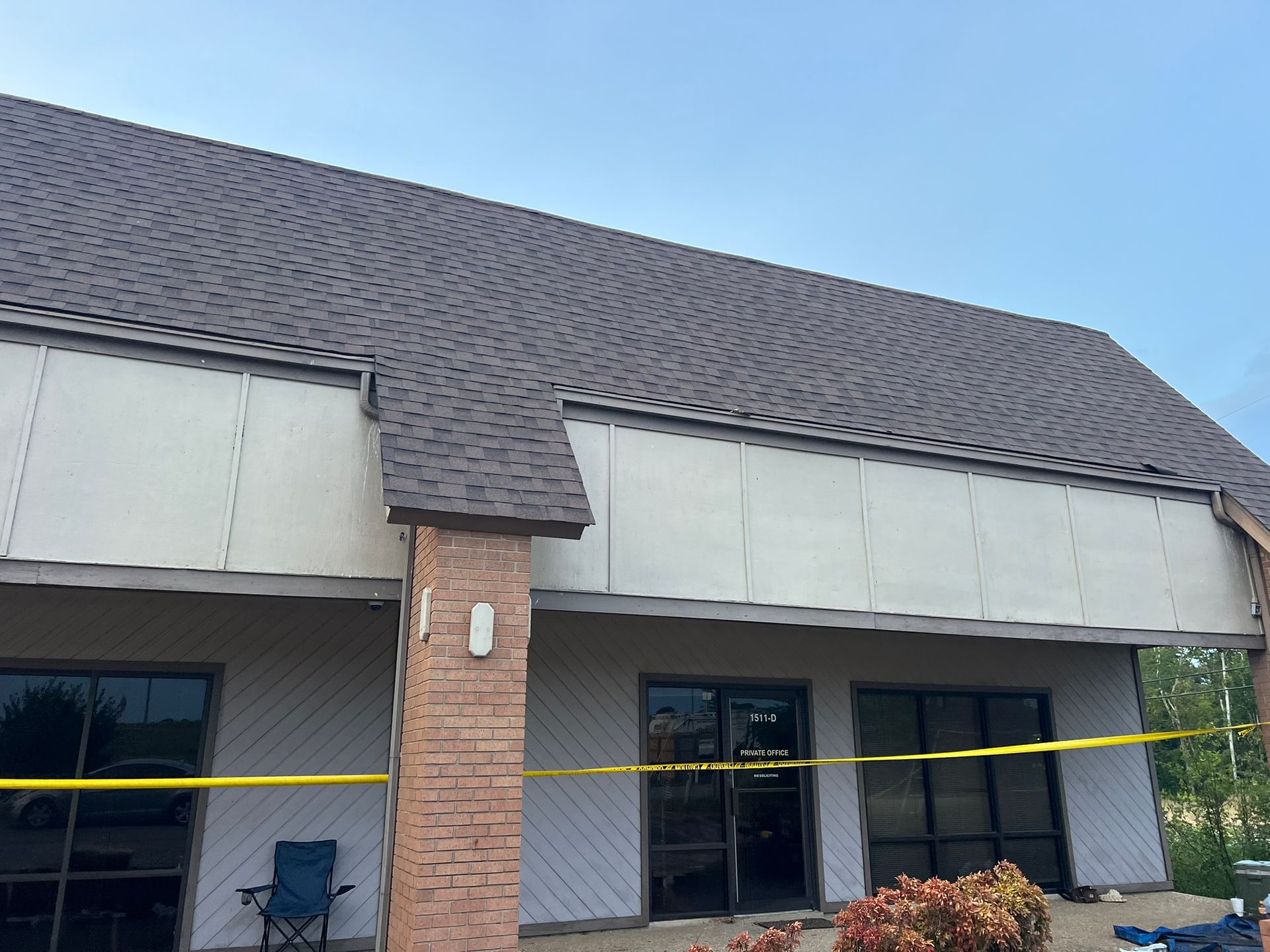 Building exterior with brown shingle roof, white paneling, and a brick pillar. Yellow caution tape is visible.