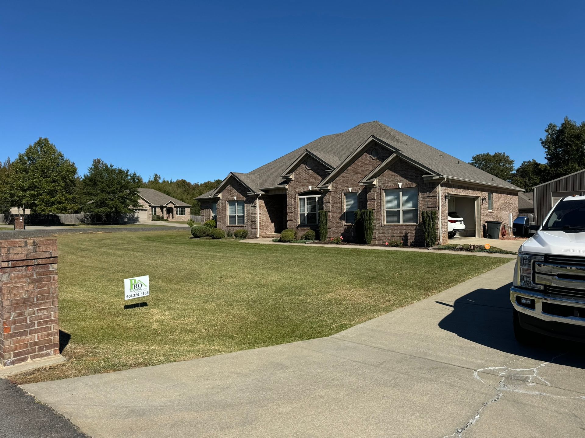 A brick house with a brown roof and a green lawn on a sunny day. A truck is parked in the driveway.