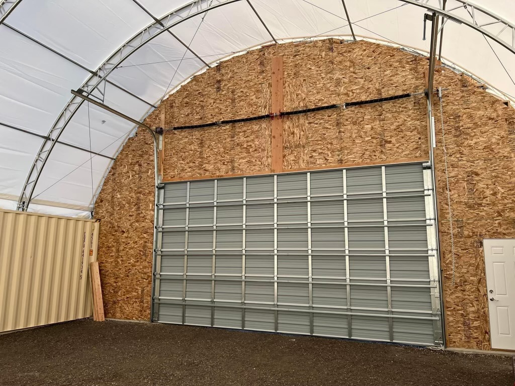 Interior of a large arched structure with a closed metal door, a tan container, and a wood panel wall.