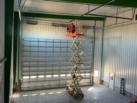 Person on scissor lift works on wiring above a large warehouse door, in a metal building.