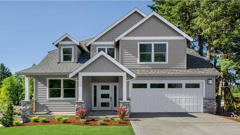 Gray two-story house with a white garage door, porch, and landscaping under a clear blue sky.