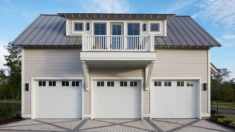 Three-car garage with a balcony above. Gray siding, white doors, and a silver metal roof.