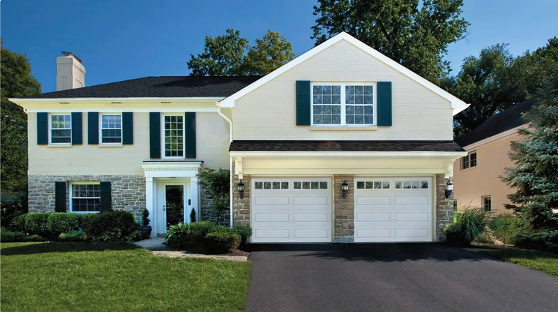 Two-story house with beige siding, stone accents, black roof, and two-car garage.
