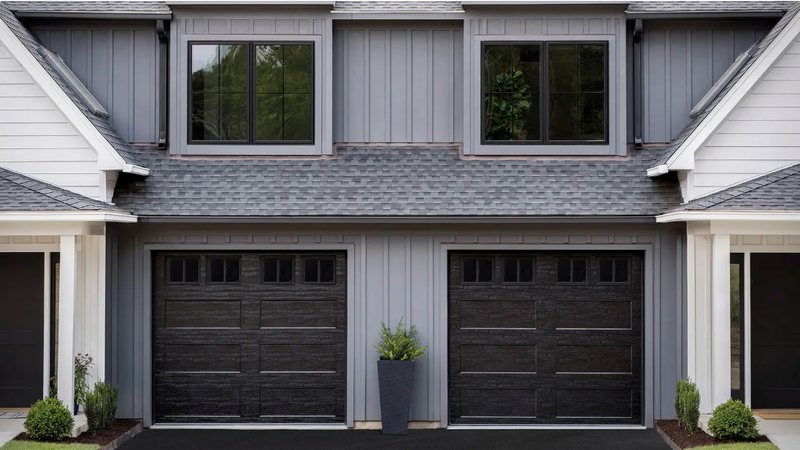Two-car garage with black doors, gray siding, two windows, and a plant.