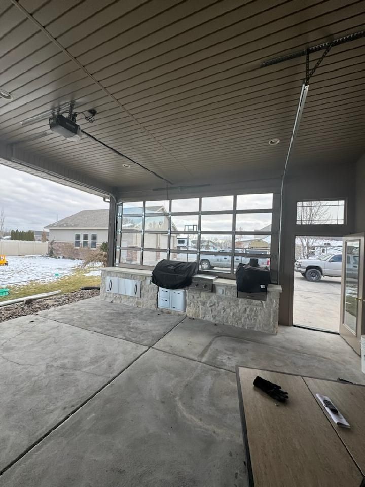 Outdoor kitchen with a grill and a glass garage door. Concrete patio. Overcast sky.