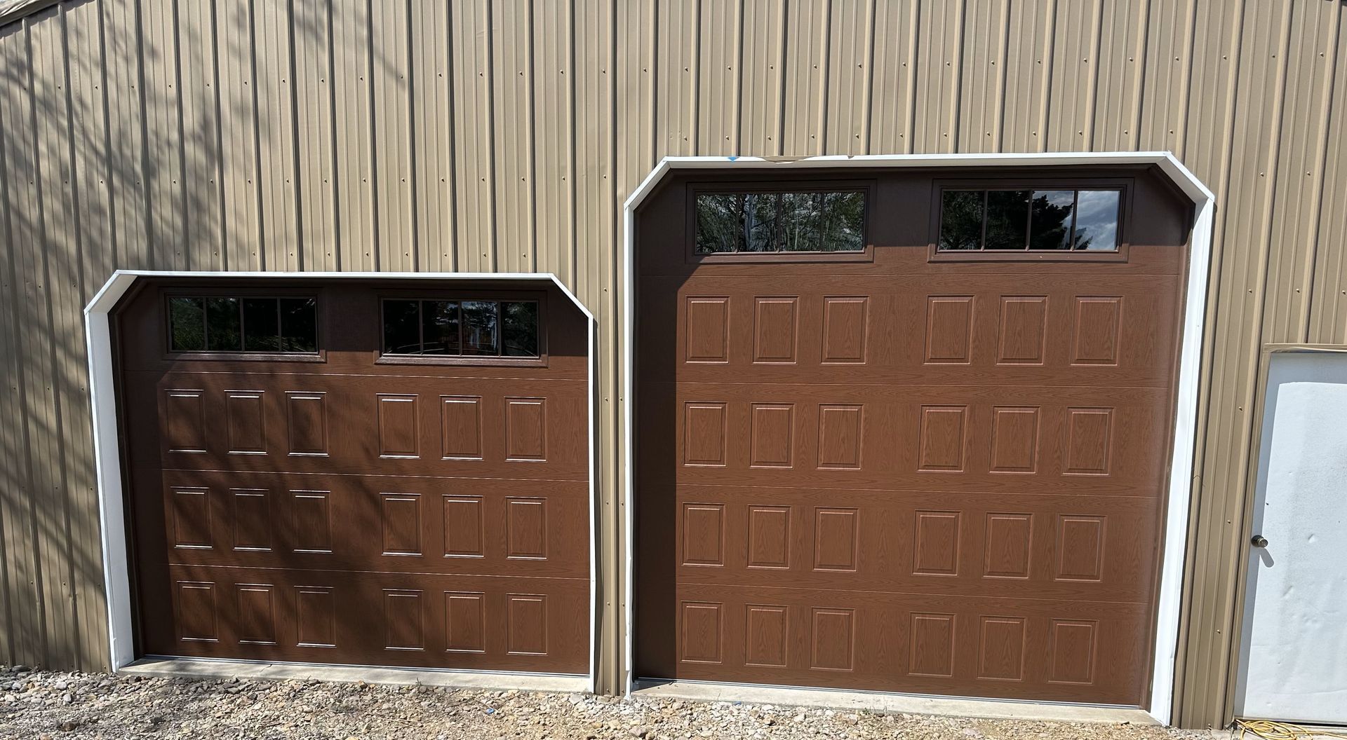Two brown garage doors with white trim, one larger than the other, on a wooden building.