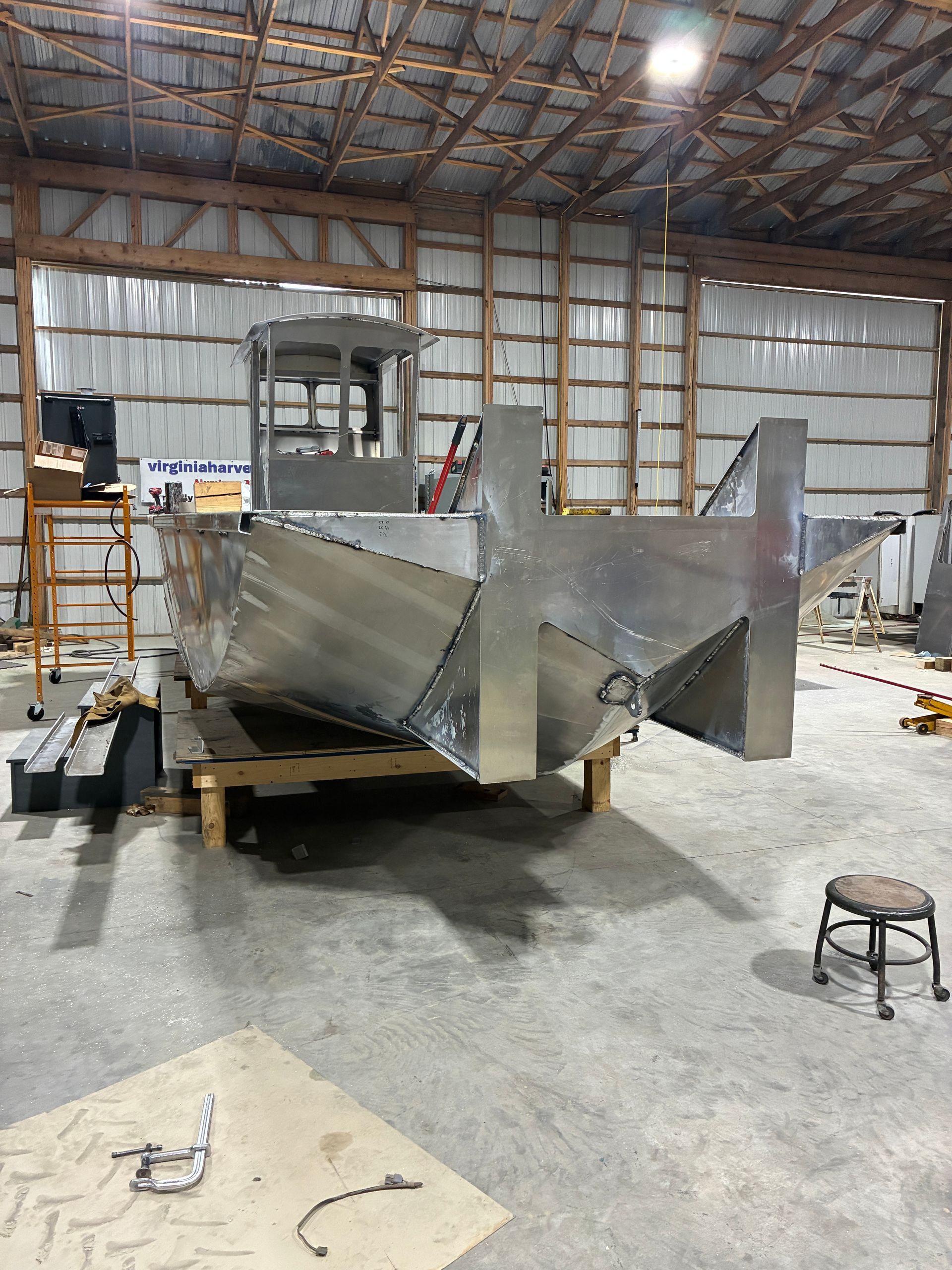 A metal boat hull under construction in a workshop, featuring a pilot house and a dual-hull design resting on supports.