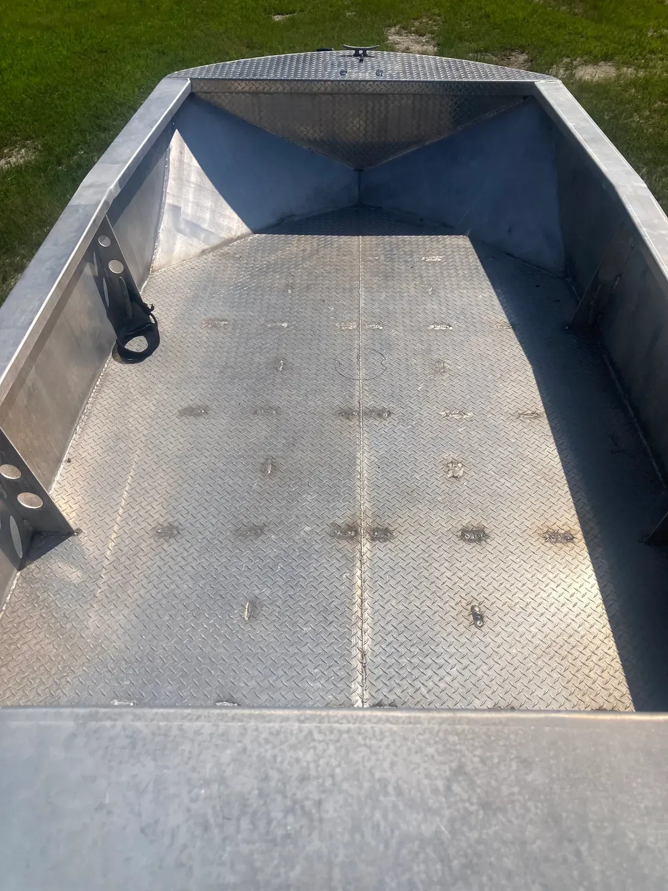 An empty aluminum boat interior with a diamond-plate floor and a bow storage compartment, viewed from the rear.
