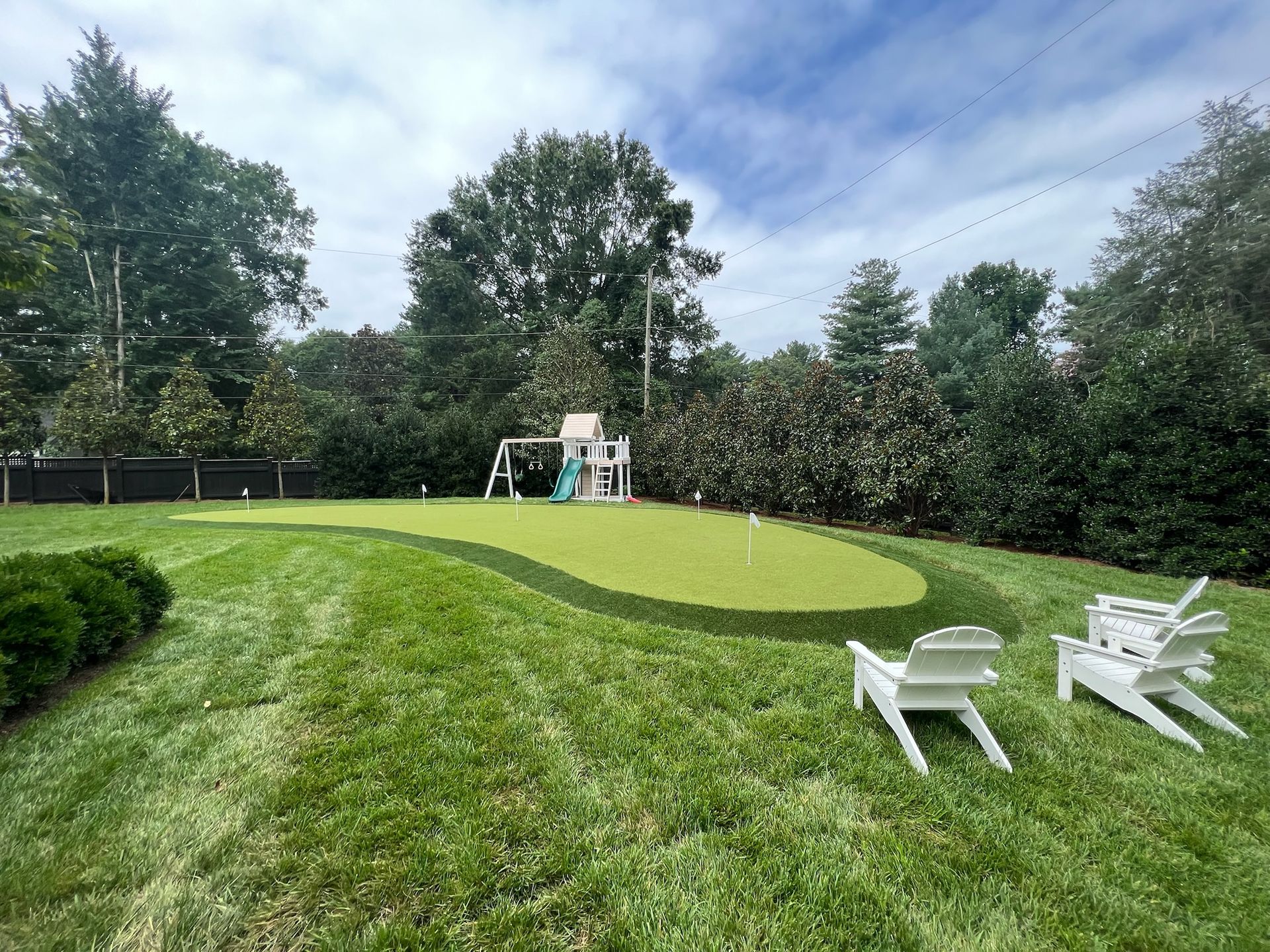 A backyard with a putting green and lawn chairs.