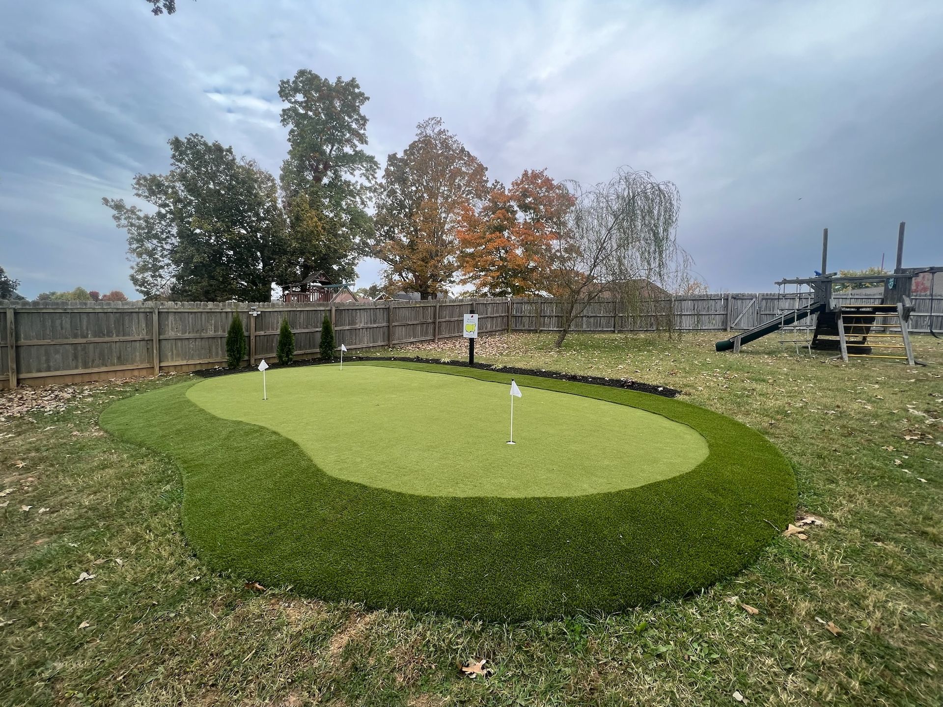 A putting green in a backyard with a playground in the background.