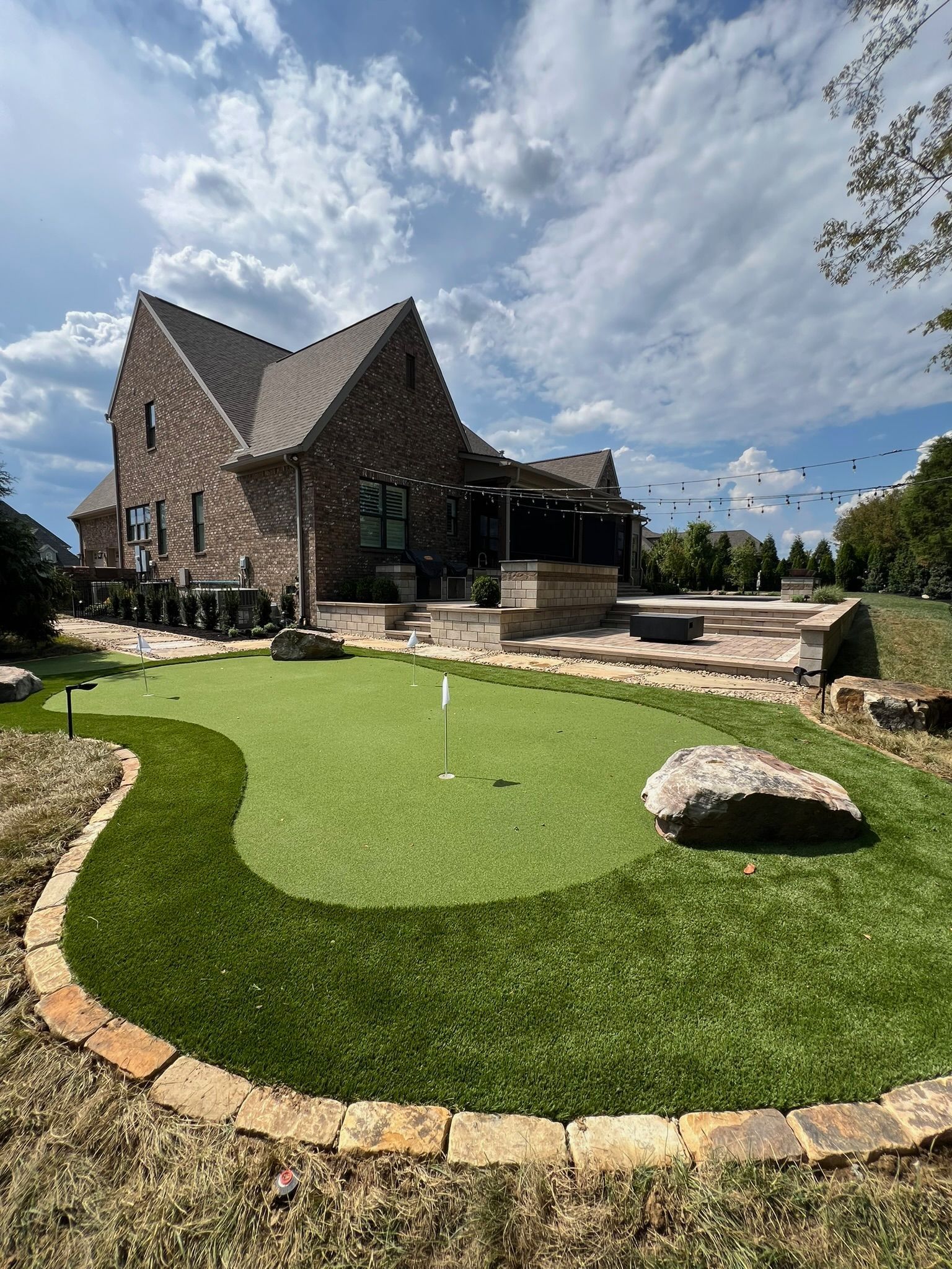 A large brick house with a putting green in front of it.