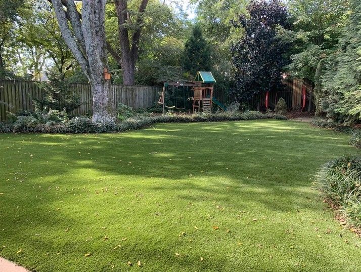 A large lush green lawn in a backyard with a playground in the background.