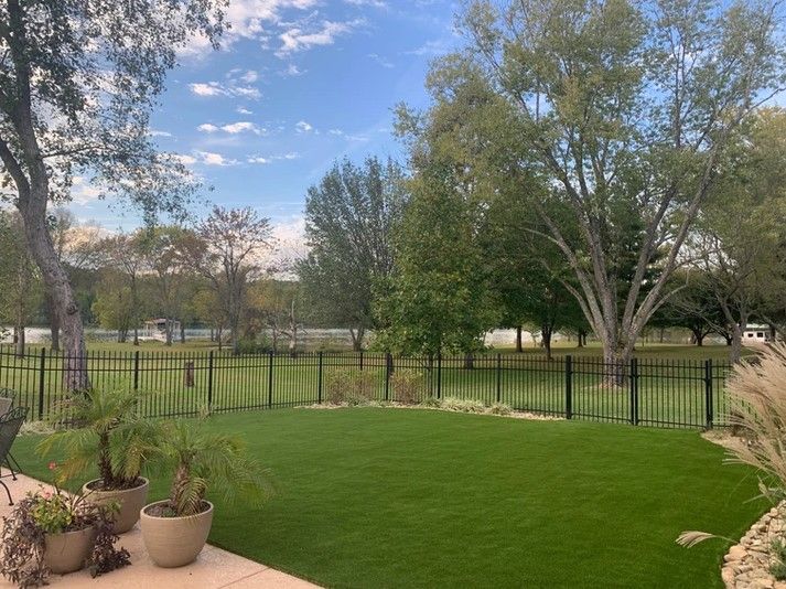A large lawn with a black fence and trees in the background.