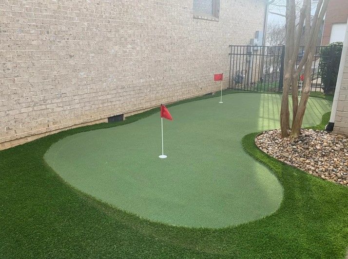 A small green putting green in front of a brick building.