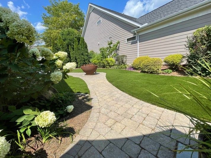 A brick walkway leading to a house with a fire pit in the backyard.