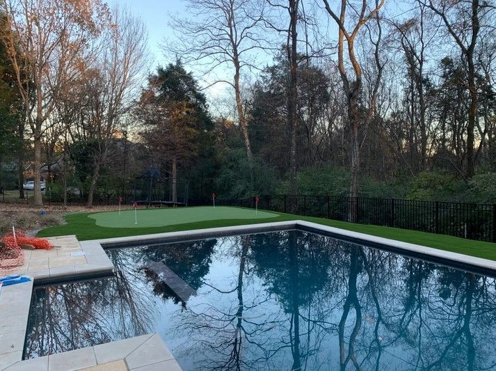 A large swimming pool with a putting green in the backyard surrounded by trees.
