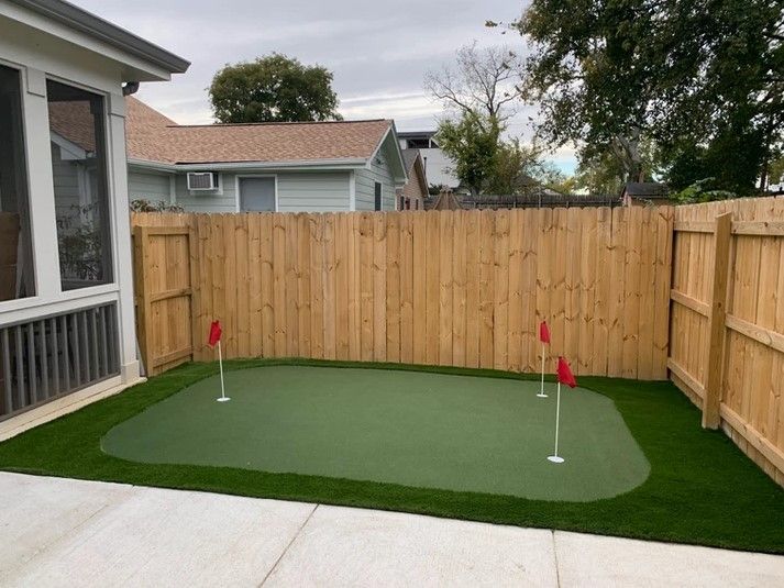 A backyard with a putting green and a wooden fence
