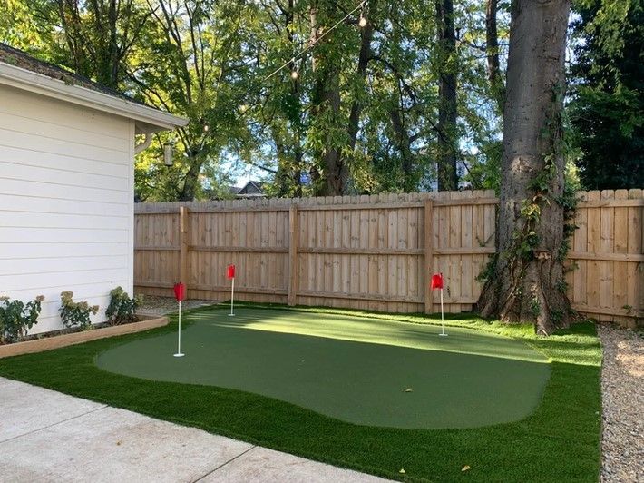 A backyard with a putting green and a wooden fence.