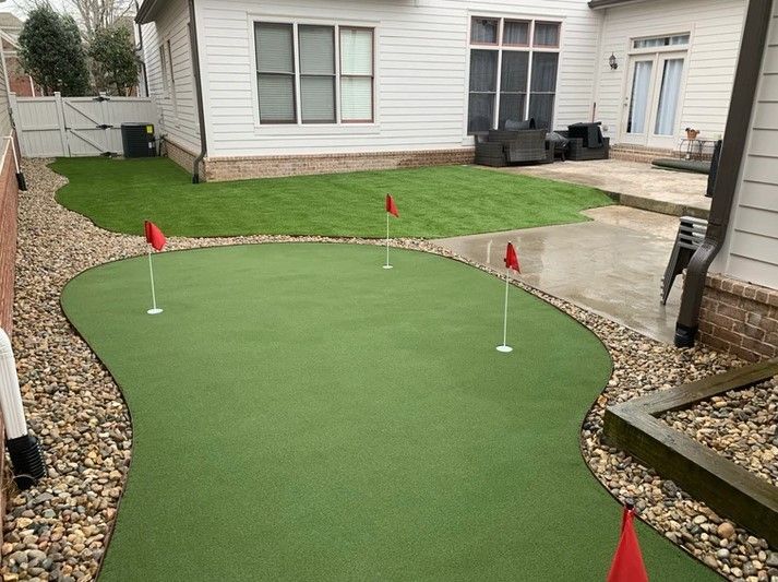 There is a putting green in the backyard of a house.