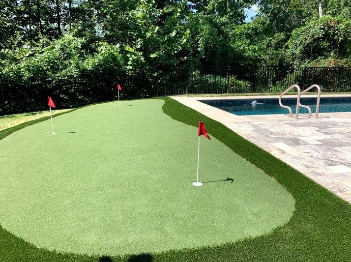 A putting green in a backyard next to a pool.