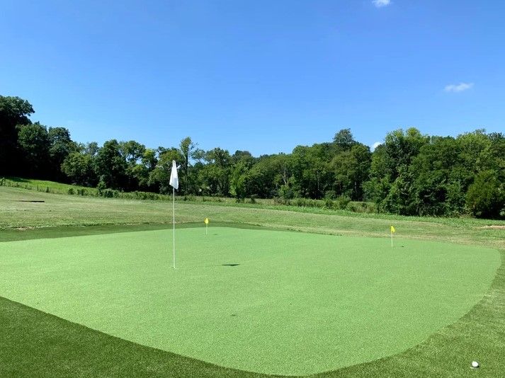 A golf course with a green and trees in the background.