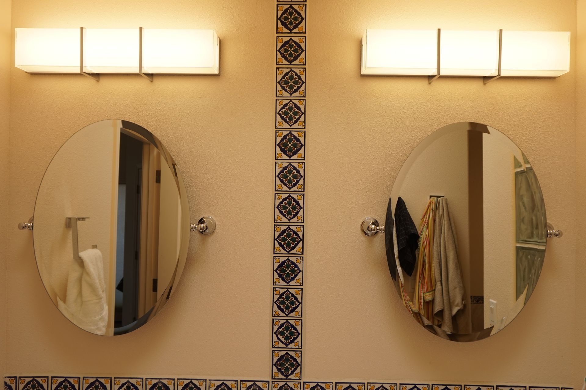 two round mirrors in a bathroom with lights above them
