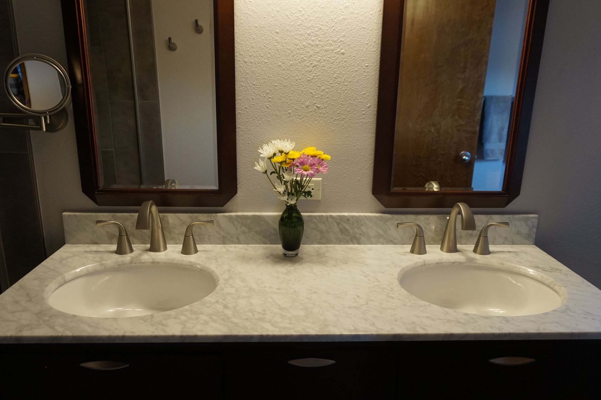 a bathroom with two sinks and two mirrors and a vase of flowers on the counter