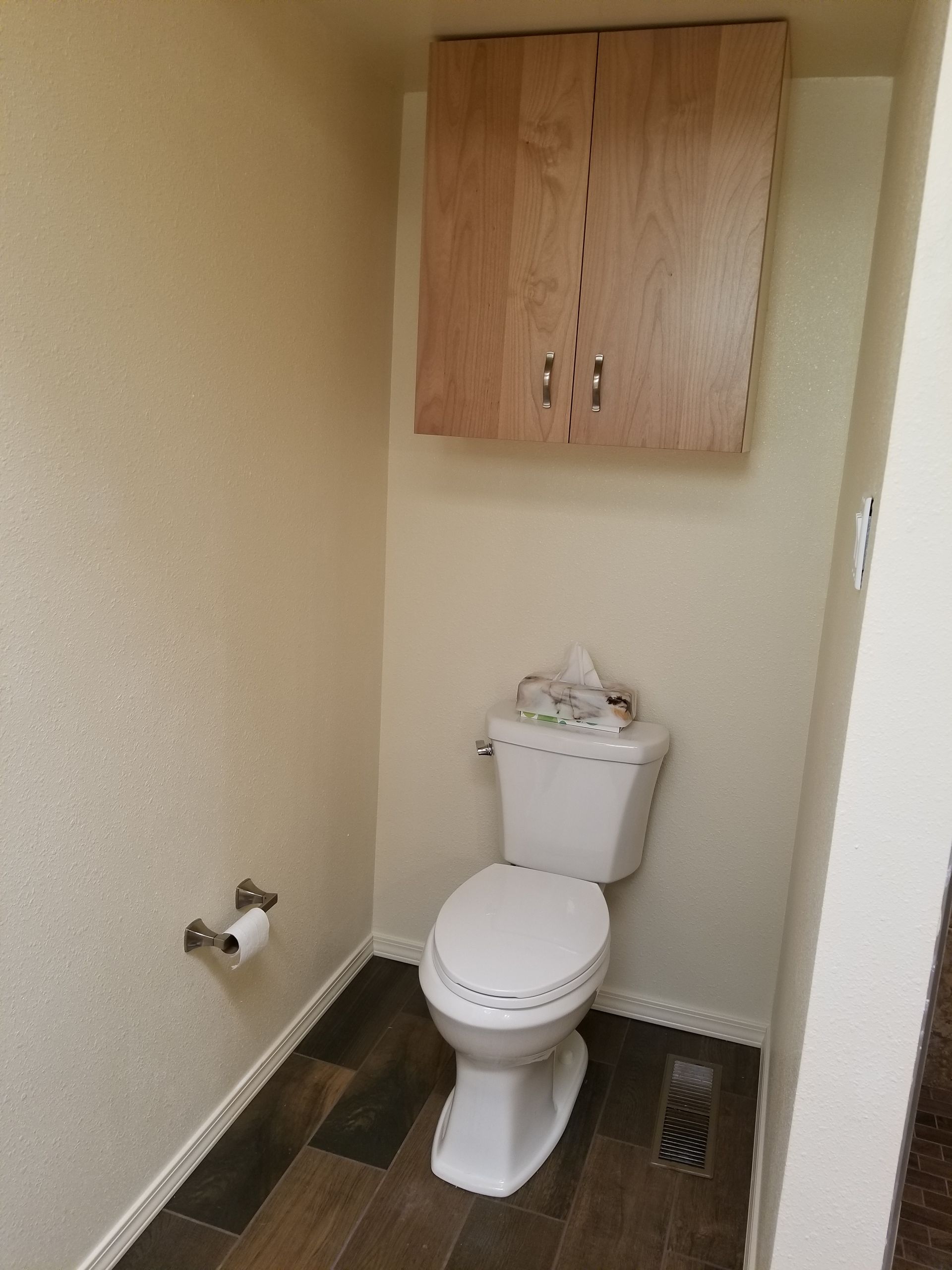 a toilet in a bathroom with a wooden cabinet above it