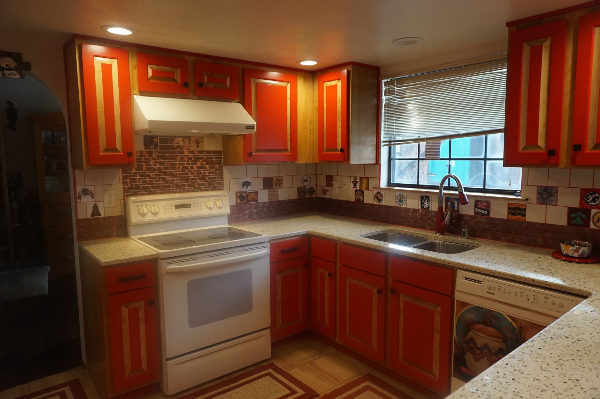 a kitchen with red cabinets, a white stove, a sink, and a window