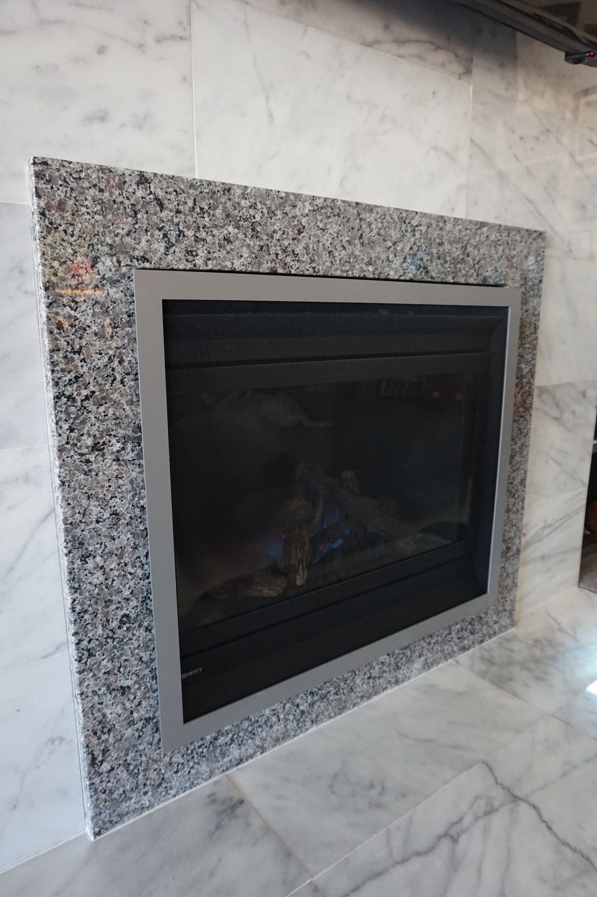 a fireplace is surrounded by marble tiles and has a stainless steel frame