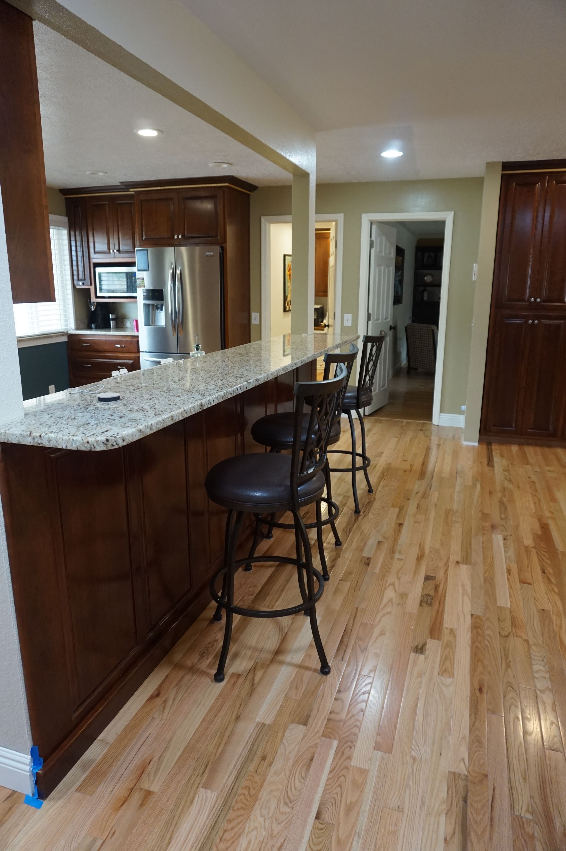 a kitchen with hardwood floors, granite counter tops, stools and a refrigerator