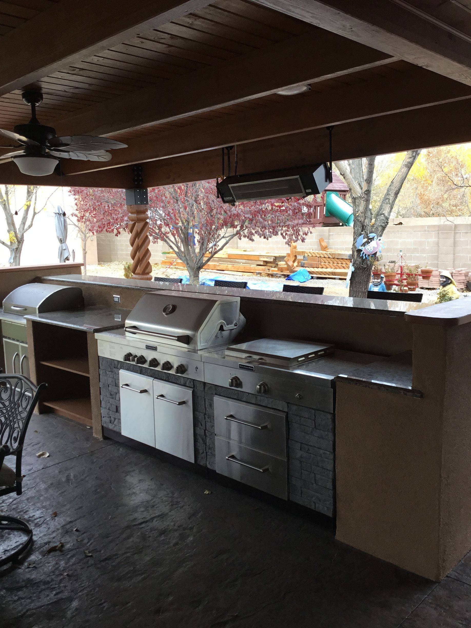 an outdoor kitchen with a grill, sink, cabinets and a ceiling fan
