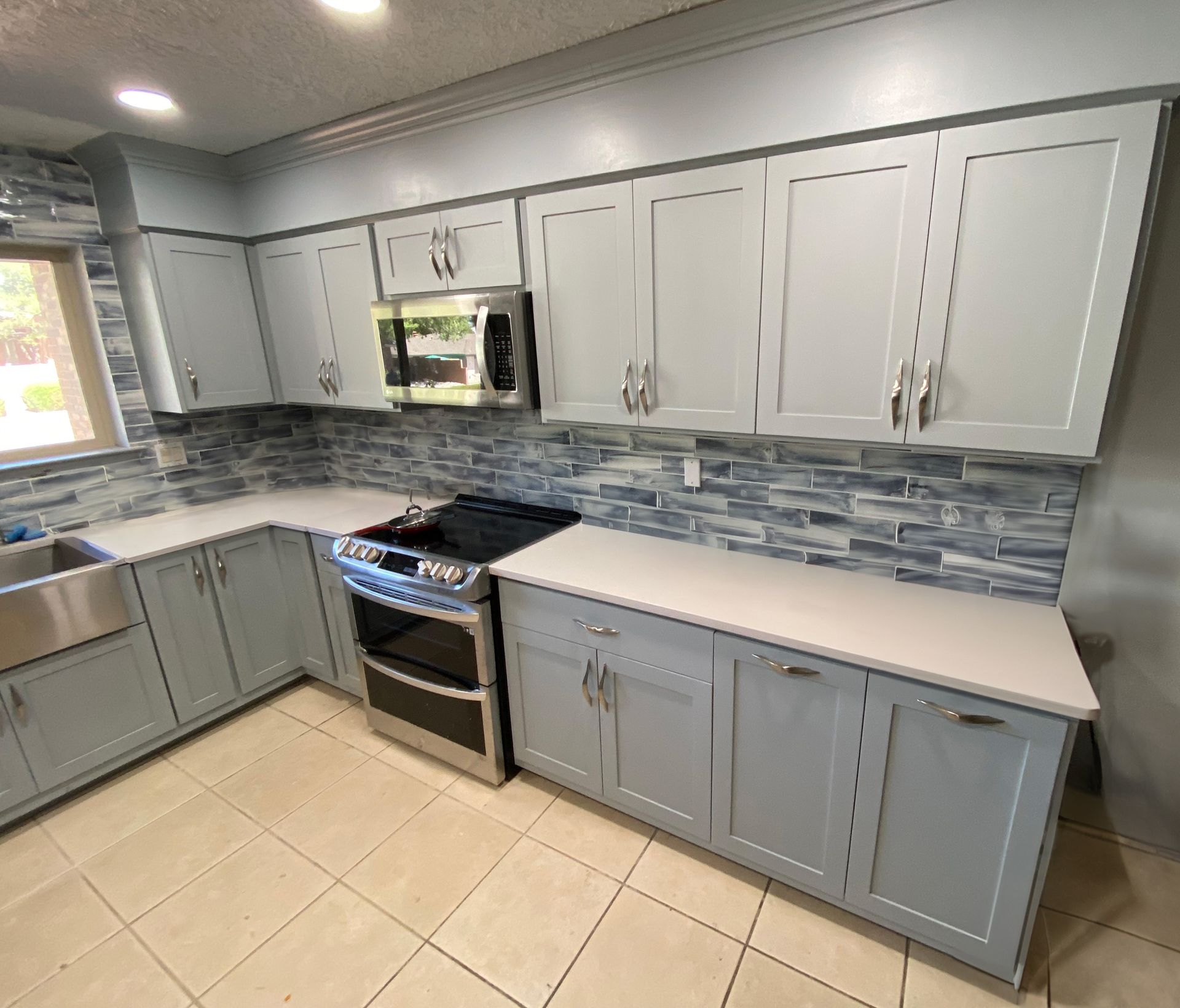 a kitchen with gray cabinets, a stove, a microwave, and a sink