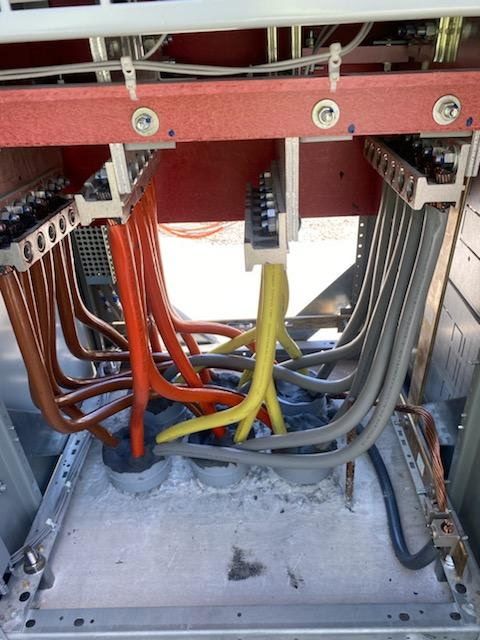 Electrical panel with red, orange, yellow, and gray cables connected to busbars.