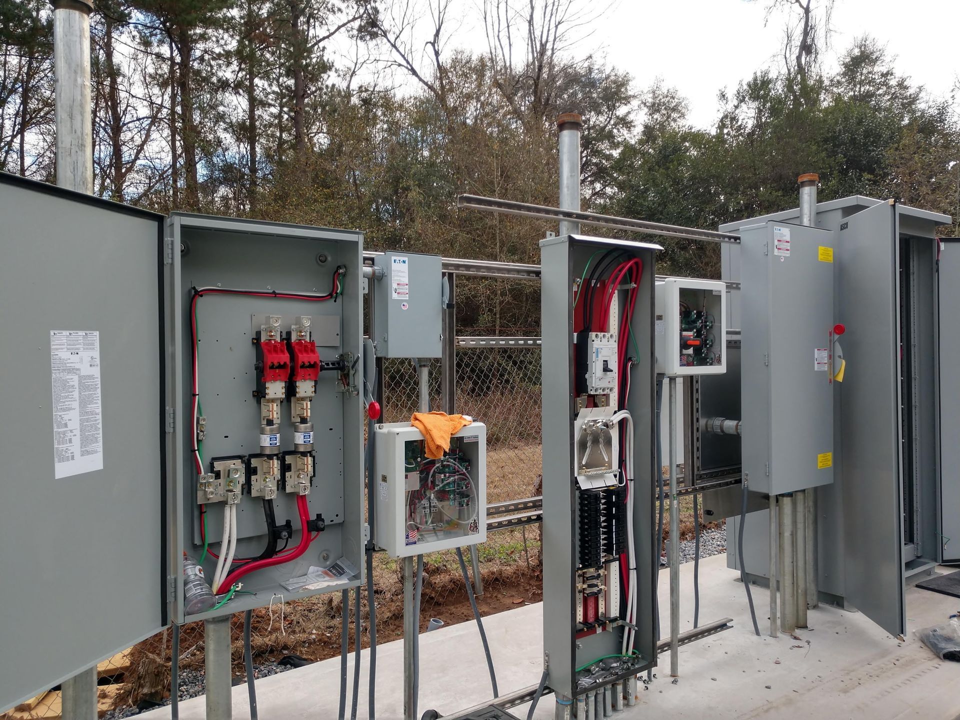 Electrical control boxes mounted outdoors, grey, open, exposing wiring and components.