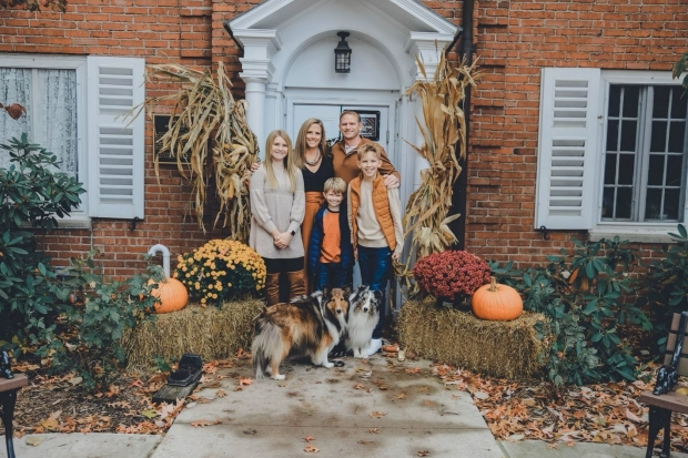 A family and their dog are posing for a picture in front of a brick house.