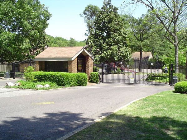 Brick guardhouse and gated entrance to a residential area, surrounded by trees and greenery.