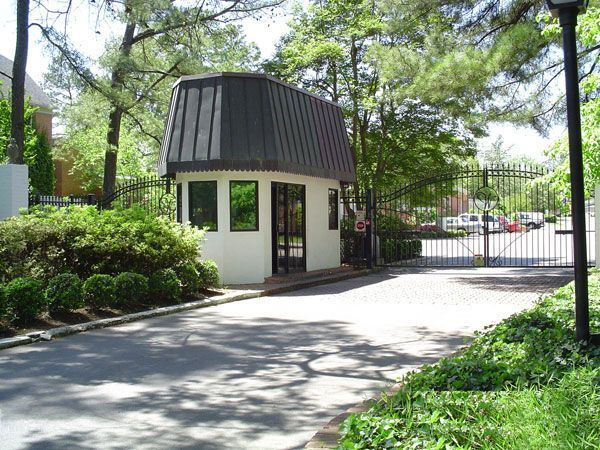 A white building with a black roof is surrounded by trees and bushes