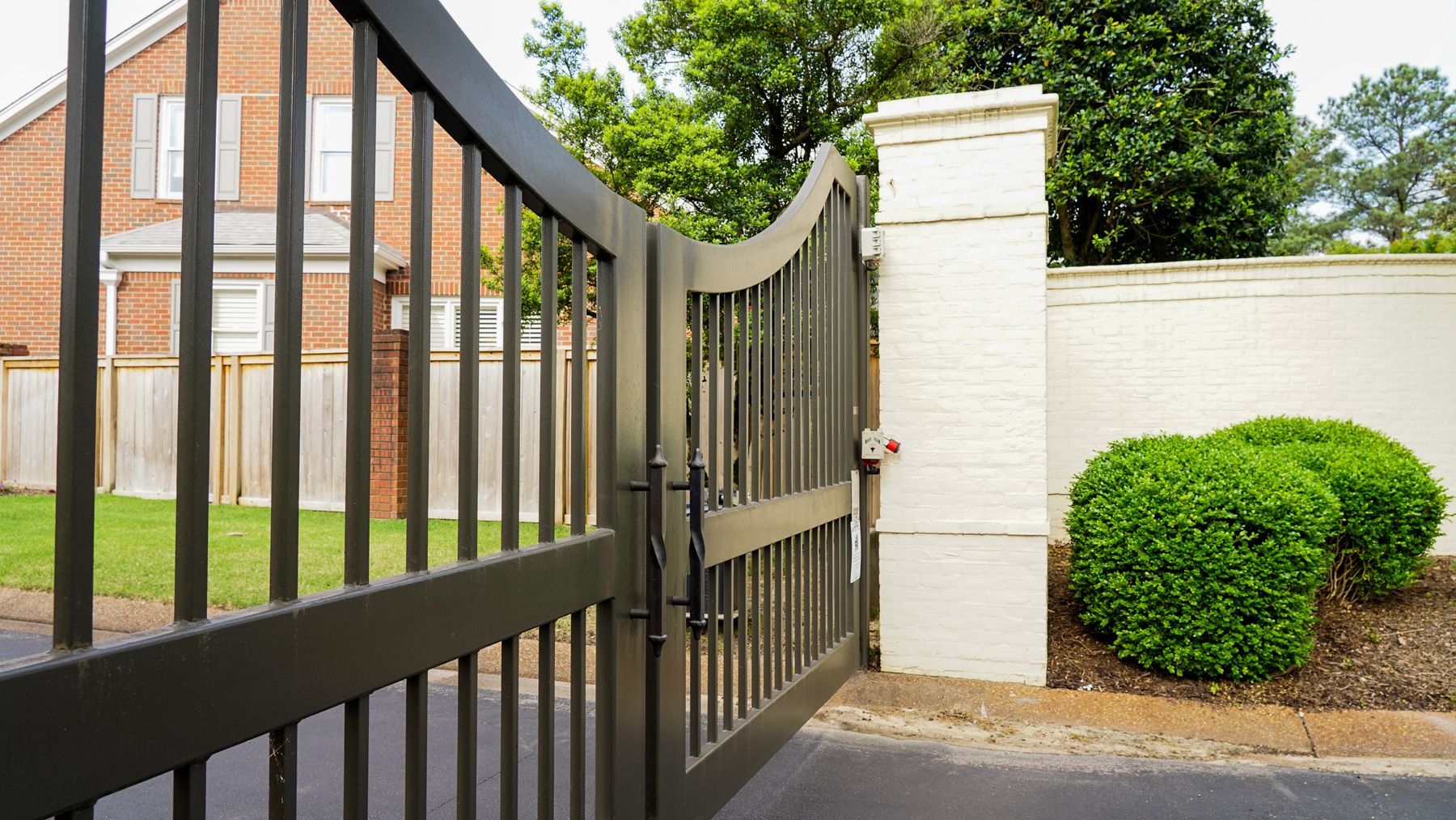A black gate is open to a driveway in front of a brick house.